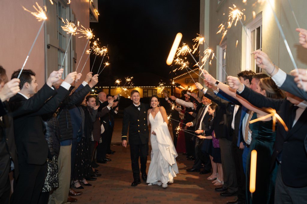 A newlywed couple walks through a joyful crowd holding sparklers at their evening wedding celebration.jpg