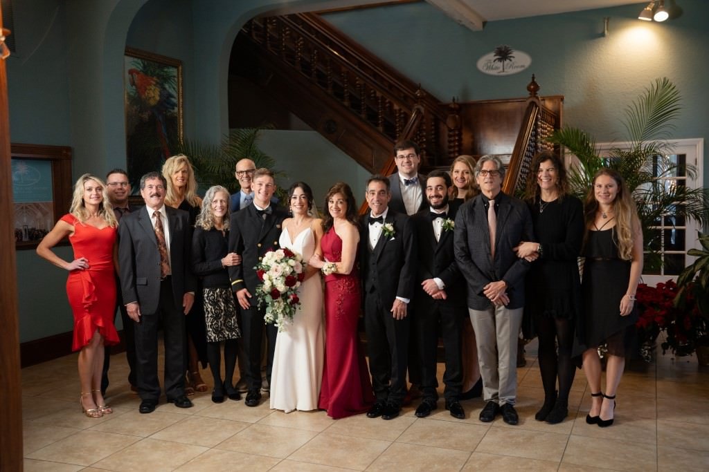 A wedding party posing together bride in white groom in black tux surrounded by friends and family in a beautifully decorated hall.jpg
