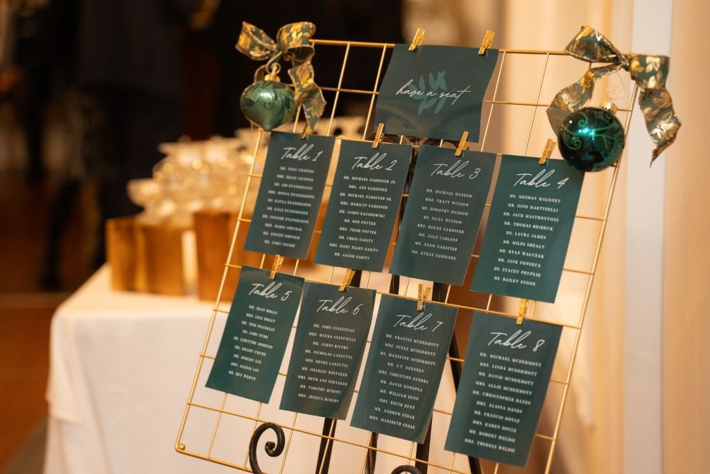 A wedding seating chart display with green cards showing table assignments adorned with gold and green decorations.jpg