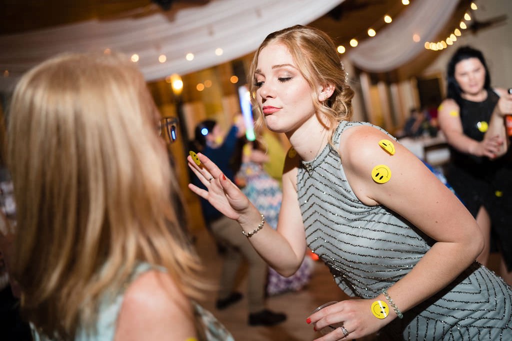 A woman at a wedding reception covered in smiley face stickers dances with a friend.jpg