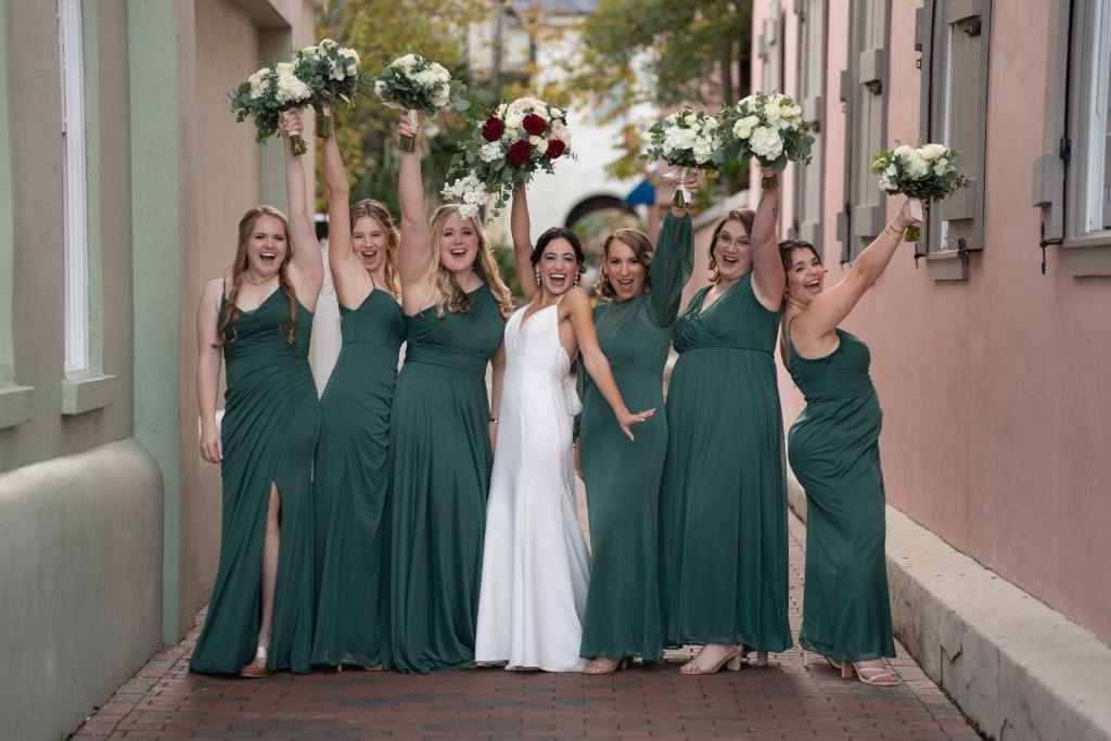 Bride and bridesmaids celebrating with bouquets in a joyful alleyway.jpg