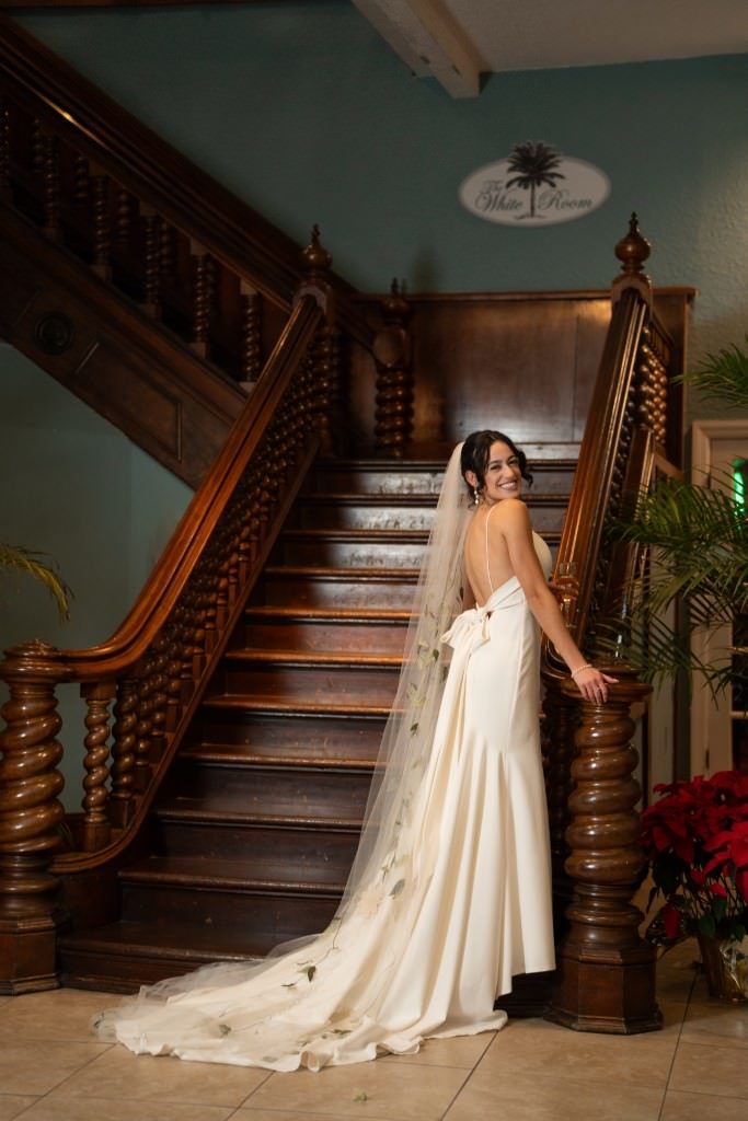 Bride in elegant white gown poses on grand wooden staircase.jpg