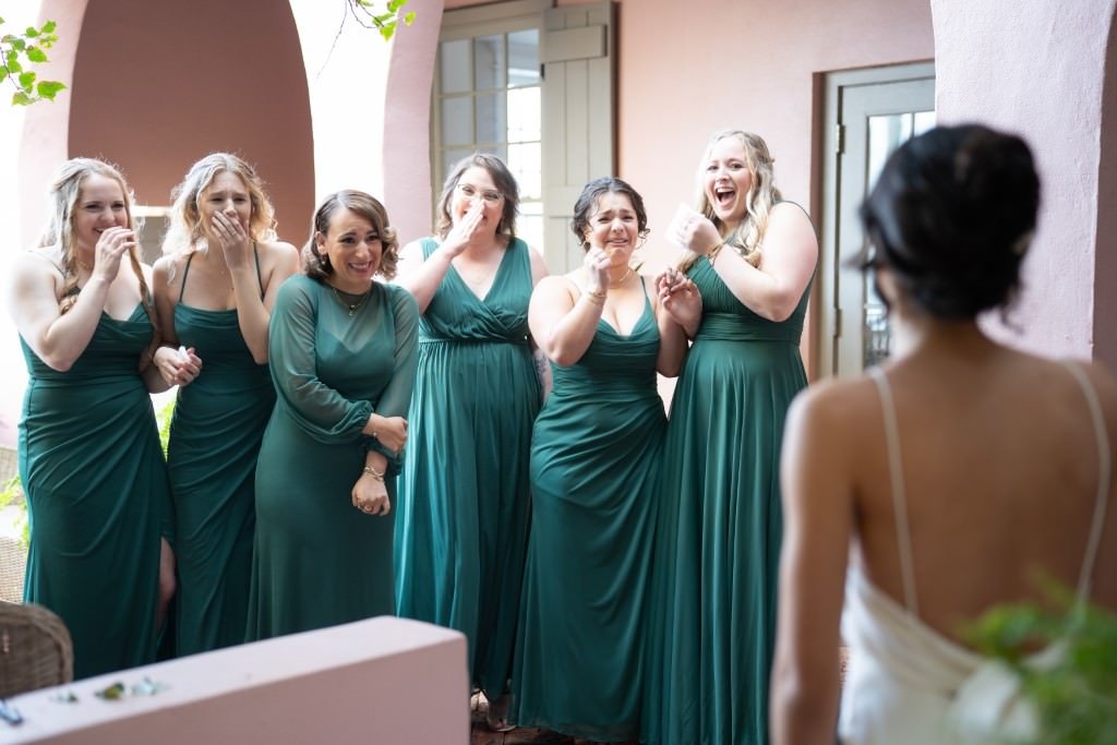 Bridesmaids react with joy and excitement as they see the bride in her wedding dress for the first time.jpg
