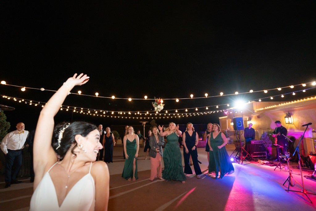 Bride tossing bouquet towards a group of excited guests under string lights at night.jpg