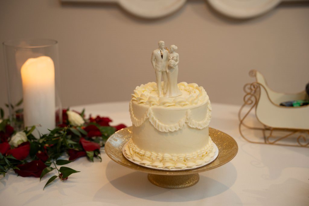 Elegant wedding cake with a bride and groom topper surrounded by romantic decor including a candle and rose petals.jpg