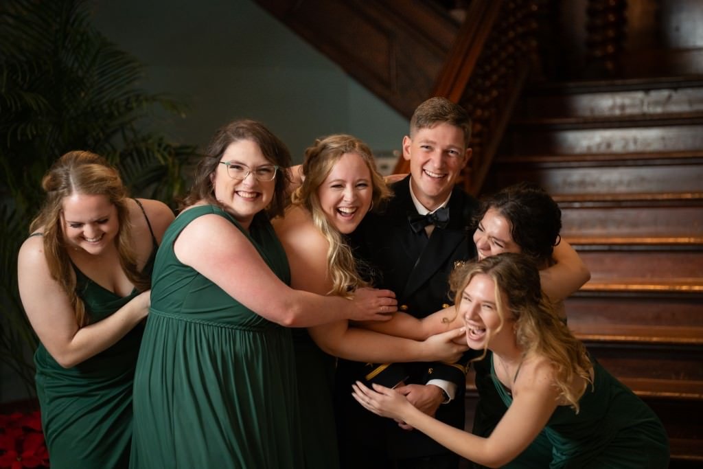 Friends in green dresses and suits share a joyful moment on the stairs laughing and hugging.jpg