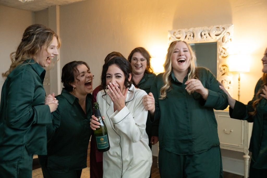 Friends share a joyous laugh with the bride to be clad in pajamas and holding a champagne bottle.jpg