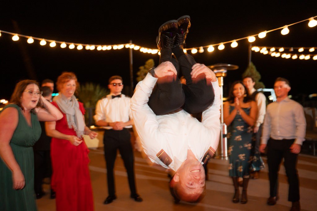 Man impressively flips in the air at an outdoor party under string lights surrounded by amazed onlookers.jpg