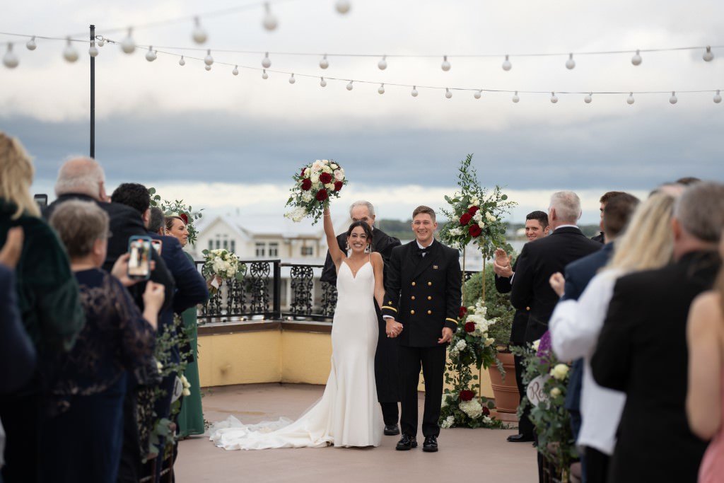 Newlyweds joyfully walk down the aisle amidst cheering guests on a beautifully decorated rooftop.jpg