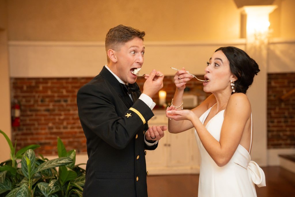 Newlyweds share a light hearted moment feeding each other cake at their reception.jpg