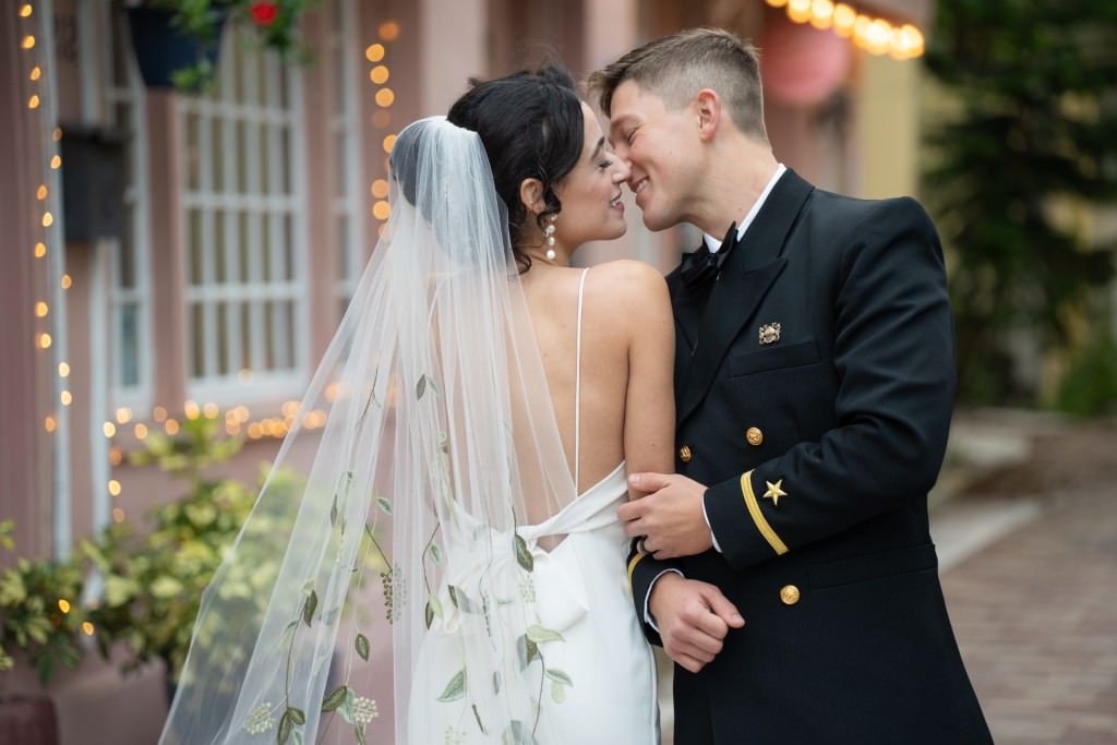 Newlyweds share an intimate moment the bride in a veil with floral accents and the groom in a formal navy uniform.jpg
