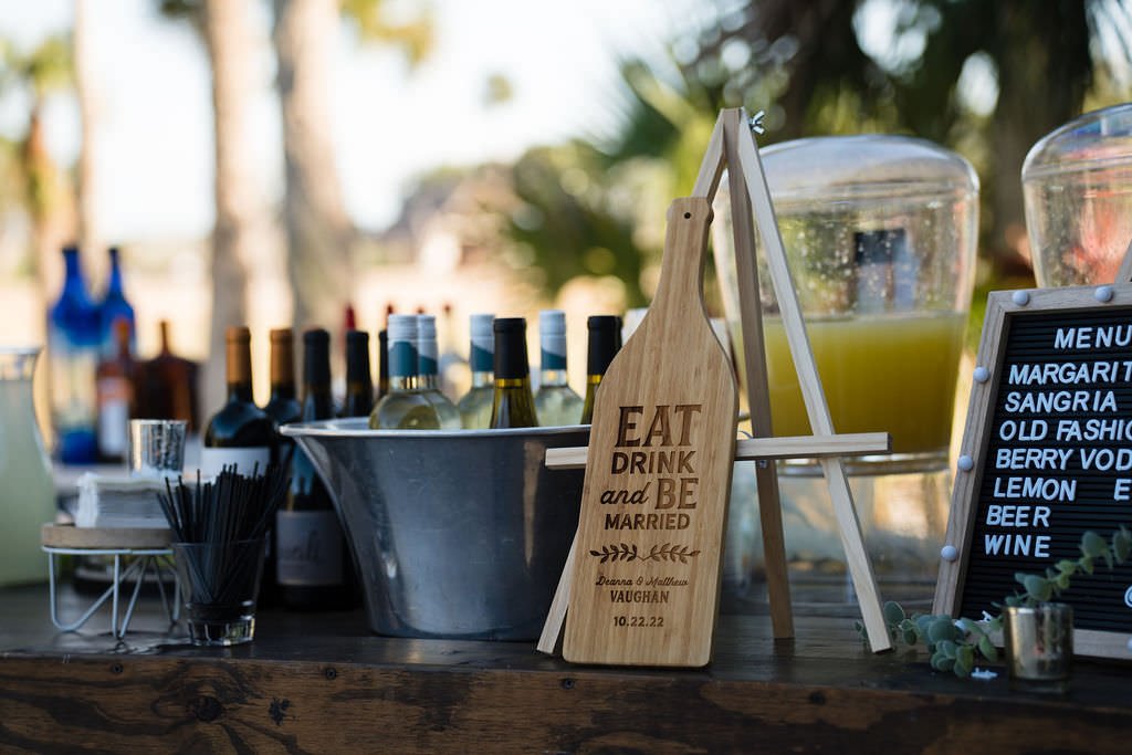 Outdoor wedding drink station with wine bottles juice dispensers and a sign saying Eat Drink and be Married.jpg