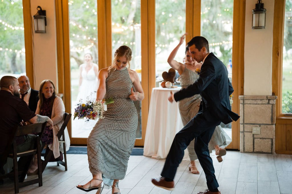 The newlyweds are having fun dancing at their reception The bride is in the background watching them.jpg