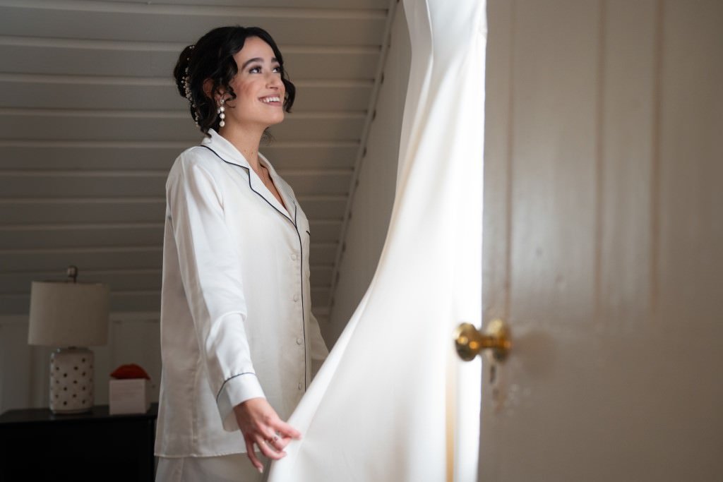 Woman smiles brightly as she gazes outside holding back a curtain.jpg